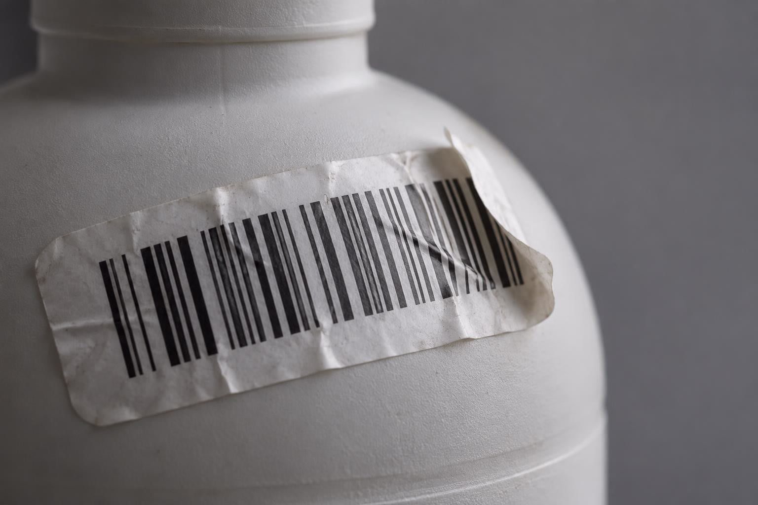A wrinkled barcode label lifting off the curved shoulder of a plastic bottle